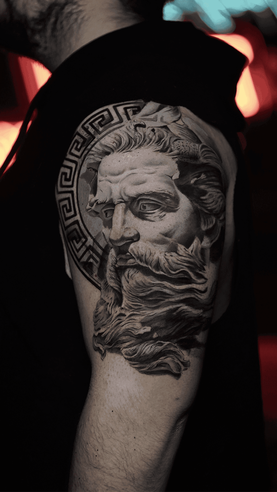Black-and-grey realism tattoo of a classical Greek statue head framed by a meander border
