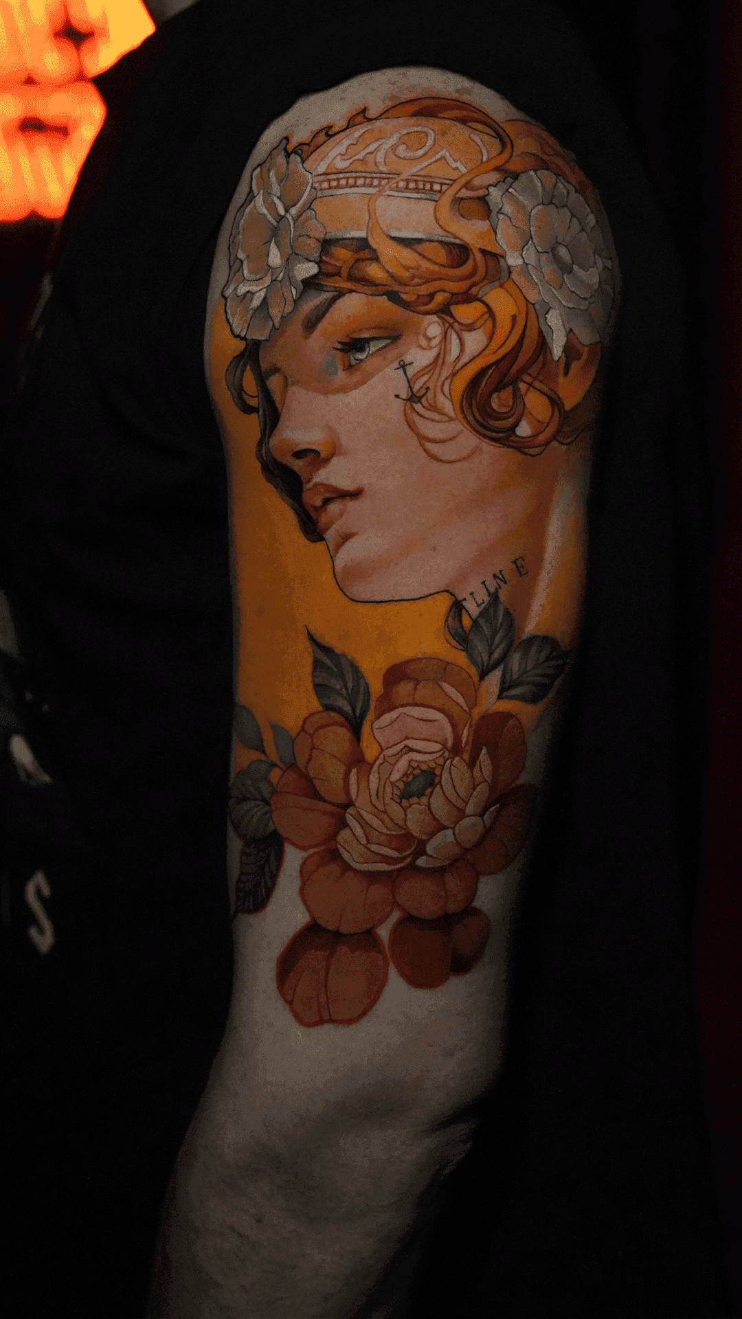 Color tattoo of a woman in an Art Nouveau-style hairpiece above peony flowers on the upper arm