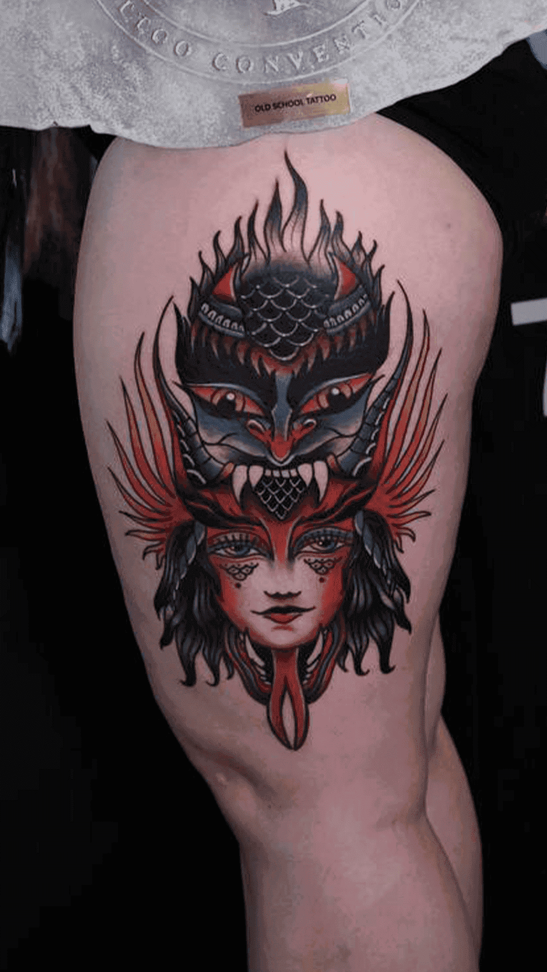 Neo-traditional color tattoo of a woman wearing a horned demon mask with flames, on the thigh