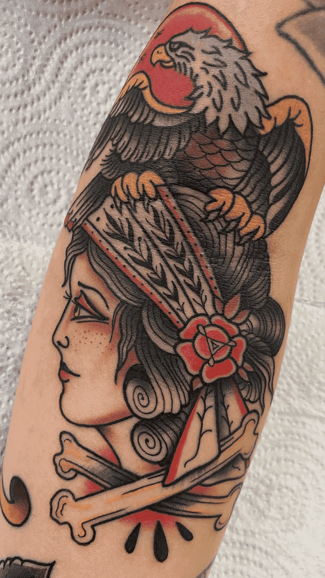 American traditional color tattoo of a woman in a rose-trimmed headscarf with an eagle and crossbones