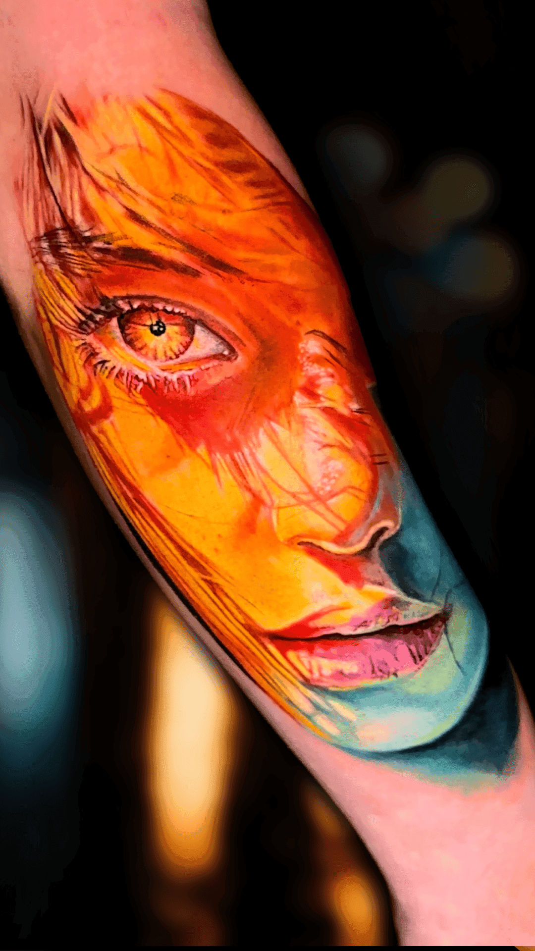 Color realism portrait of a woman's face in vivid orange and blue tones on a forearm